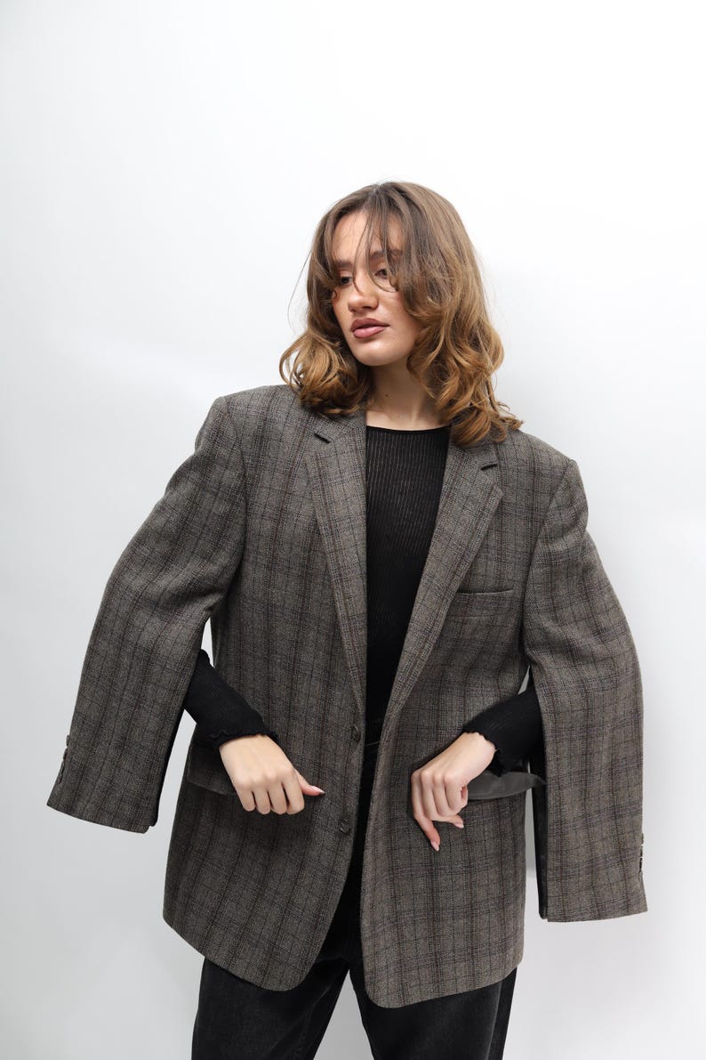 May include: A brown plaid blazer with a classic design. The blazer features a notched lapel, two front pockets, and button closures. The model is wearing a black long-sleeve top and dark jeans. A versatile piece for any wardrobe.
