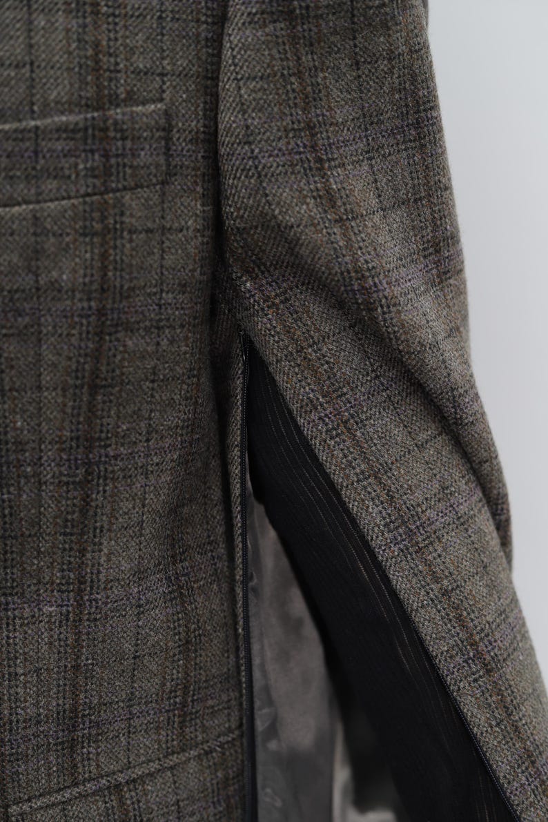 May include: Close-up of a tweed blazer in brown, grey, and blue hues. The fabric features a plaid design. The interior lining is black. A pocket of the blazer is visible.
