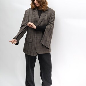 May include: A brown plaid blazer, black sweater, and black trousers. The blazer features a classic design with a notched lapel and two front pockets. The trousers are dark wash denim. The person is wearing black heeled boots.