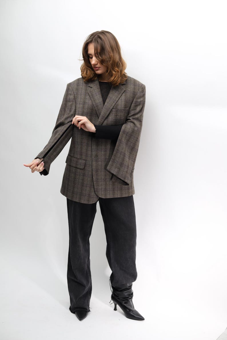 May include: A brown plaid blazer, black sweater, and black trousers. The blazer features a classic design with a notched lapel and two front pockets. The trousers are dark wash denim. The person is wearing black heeled boots.