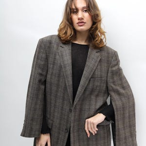 May include: A brown plaid blazer with a classic design. The blazer features a notched lapel, a two-button closure, and a single chest pocket. The sleeves are long with buttoned cuffs. The blazer is worn over a black top and black trousers.