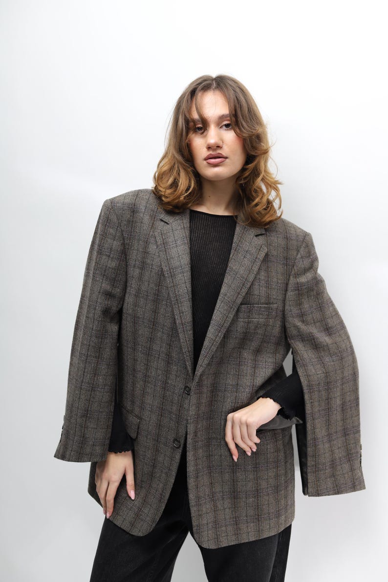 May include: A brown plaid blazer with a classic design. The blazer features a notched lapel, a two-button closure, and a single chest pocket. The sleeves are long with buttoned cuffs. The blazer is worn over a black top and black trousers.
