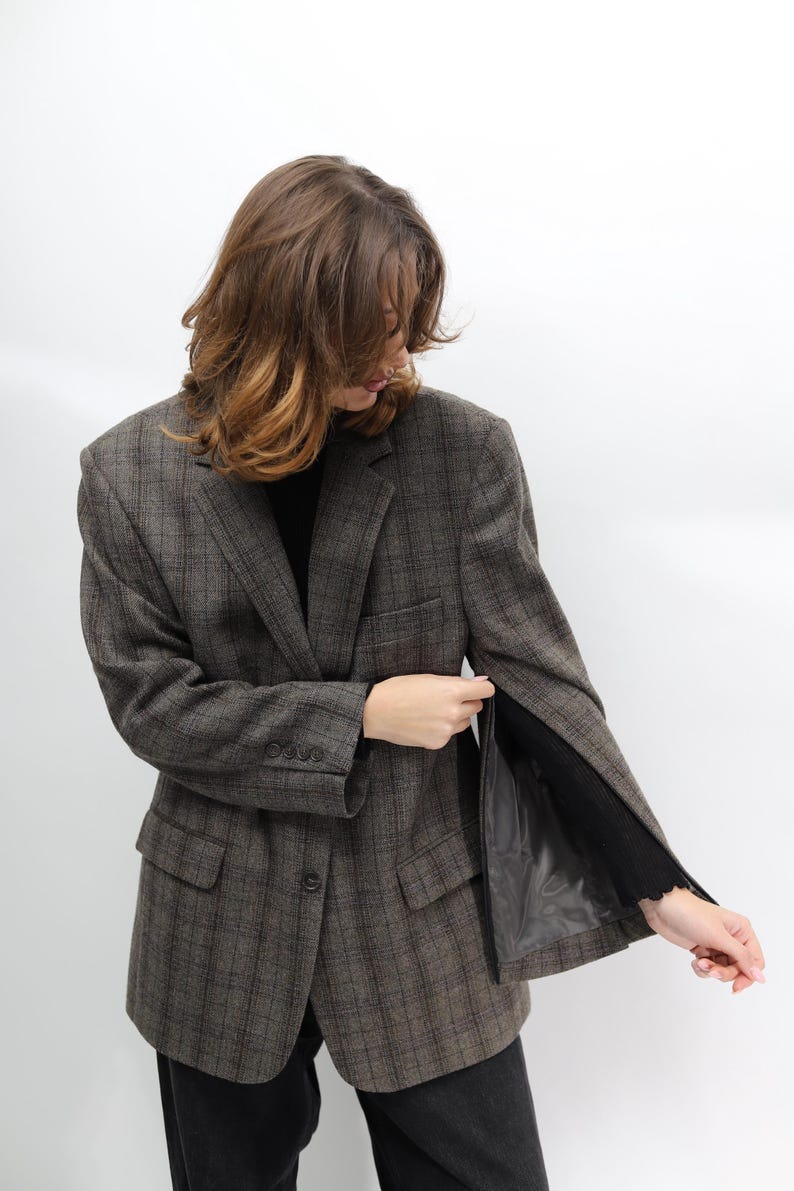 May include: A brown plaid blazer with a classic design. The blazer features a notched lapel, front pockets, and a button closure. The sleeves are long and the interior lining is black. The blazer is worn over a black top.