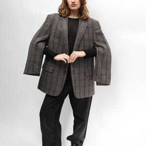 May include: A brown plaid blazer, black top, and black jeans. The blazer features a classic design with a notched lapel and two front pockets. The jeans are a dark wash and have a relaxed fit. The model is wearing black boots.
