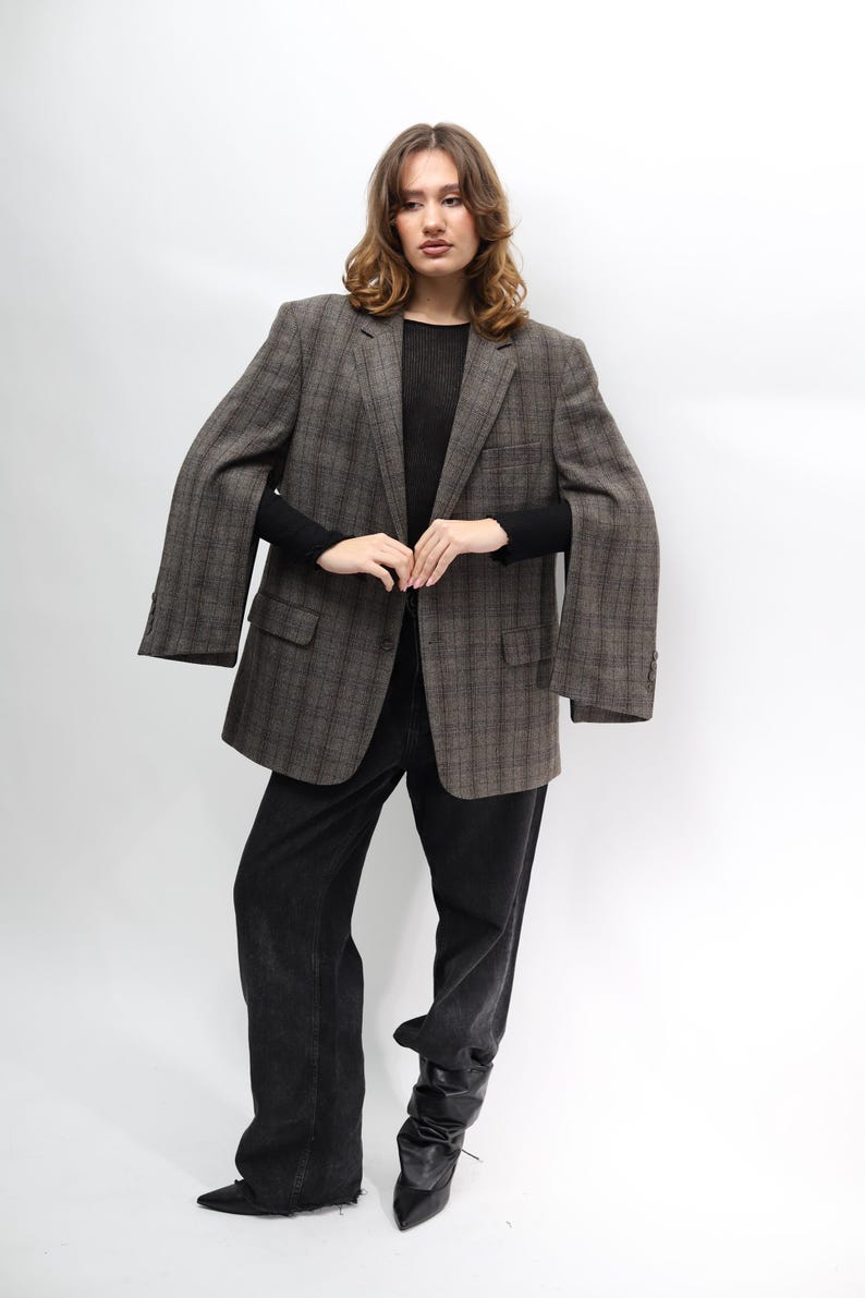 May include: A brown plaid blazer, black top, and black jeans. The blazer features a classic design with a notched lapel and two front pockets. The jeans are a dark wash and have a relaxed fit. The model is wearing black boots.