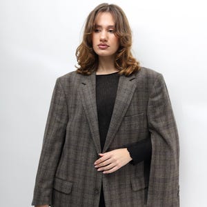 May include: A brown checked blazer with a classic design. The blazer features a notched lapel, two front pockets, and a single-button closure. The model is wearing a black top and black trousers. A versatile piece for any wardrobe.