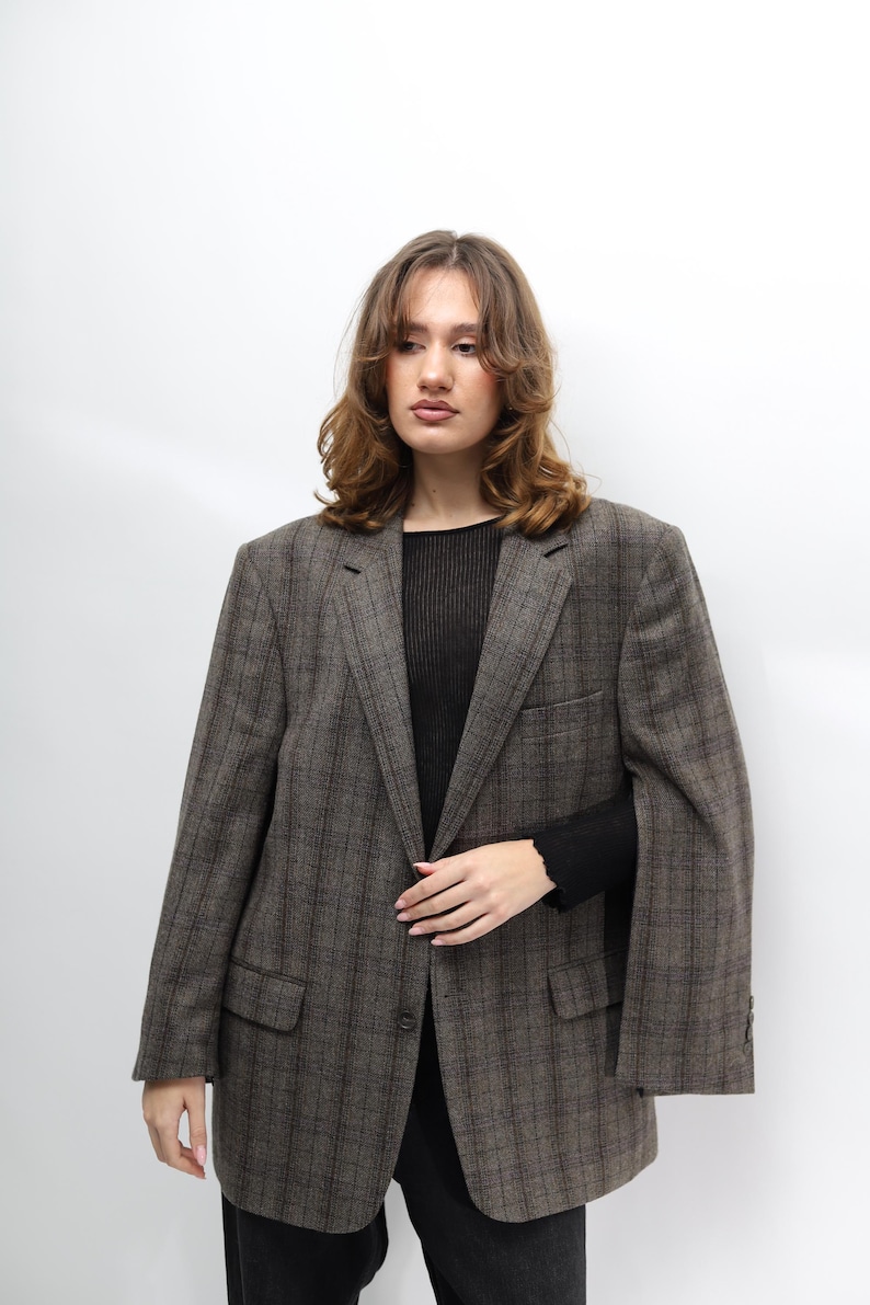 May include: A brown checked blazer with a classic design. The blazer features a notched lapel, two front pockets, and a single-button closure. The model is wearing a black top and black trousers. A versatile piece for any wardrobe.