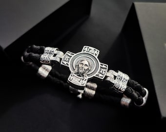 Uma pulseira de prata com imagens de Jesus, São Miguel, Santa Maria, São Nicolau e São Jorge, feita de couro escurecido.