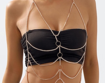May include: A gold-toned body chain with sparkling rhinestones. The chain features a halter-style design with multiple strands cascading down the chest and torso. The body jewelry includes circular accents and is worn over a black tube top.