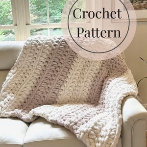 May include: A cream and mauve chunky knit blanket with a ribbed pattern, draped over a white sofa. The image includes the text "Crochet Pattern" in a circular design. The blanket is a cozy home textile.