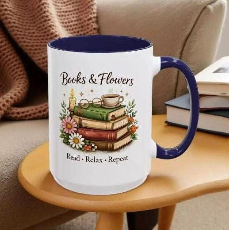 A white and blue mug with a printed design of books and flowers, sitting on a wooden table.