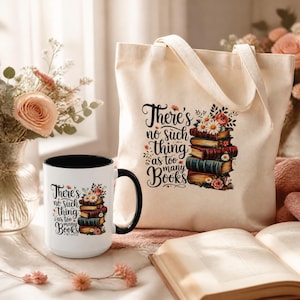 May include: A white ceramic mug with a black handle and a matching off-white canvas tote bag, both featuring a graphic of stacked books, flowers, and the text "There's no such thing as too many Books" in a black script and serif font.