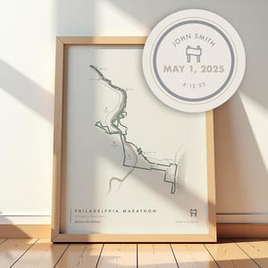 May include: Framed print of the Philadelphia Marathon course map, with the text "PHILADELPHIA MARATHON" and "26.2 mi (42.195 km)". A circular graphic displays "JOHN SMITH", "MAY 1, 2025", and "4:12:53". The frame is light wood.