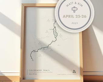 May include: A framed map print of the Colorado Trail in a light wood frame. The map features a black line route, mountain icons, and text reading Colorado Trail, 486mi (783 km). A circular overlay displays Matt & Kim, April 25-26, 2023.