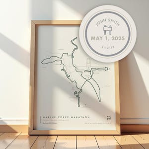 May include: A framed print depicting the Marine Corps Marathon route in Washington, D.C. The map features a minimalist design with a light backdrop and dark green lines. A circular design with the name "John Smith" and the date "May 1, 2025" is in the upper right.