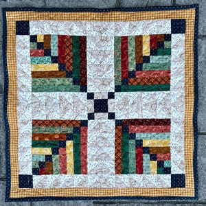 Peut inclure: Un quilt patchwork carré présentant un motif en blocs de cabane en rondins avec des sections alternées de tissu crème à motifs floraux bruns et des bandes de tissu à motifs rouges, verts, jaunes et bleu marine, bordé d'un vichy jaune.