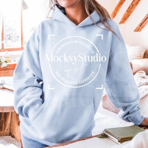 Puede incluir: Una sudadera con capucha azul claro con un bolsillo blanco y un logotipo circular blanco que dice "Mocksy Studio Art" con el texto "Alta resolución garantizada" alrededor del círculo.
