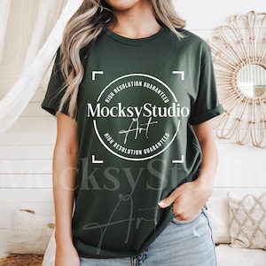 Puede incluir: Una mujer lleva una camiseta verde oscuro con un logotipo circular blanco que dice "Alta resolución garantizada" y "MocksyStudio Art".