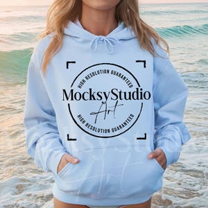 Puede incluir: Una sudadera con capucha azul claro con un logotipo circular negro que dice "MocksyStudio Art" y "High Resolution Guaranteed" alrededor del círculo.