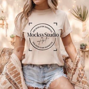 Könnte beinhalten: Eine Frau trägt ein beiges T-Shirt mit einem schwarzen Kreis-Motiv, auf dem "MocksyStudio" und "High Resolution Guaranteed" steht. Sie trägt Jeans-Shorts und einen braunen und beigefarbenen gemusterten Schal.