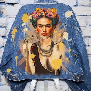 May include: A blue denim jacket with a painted image of Frida Kahlo on the back. The image is in a colorful style with yellow paint splatters.