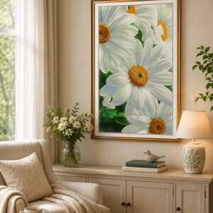 Op de afbeelding: Een verticale rechthoekige kunstprint voor aan de muur met een close-up compositie van witte madeliefjes met felgele harten. Het kunstwerk is ingelijst in een dunne goudkleurige lijst met een witte passe-partout.