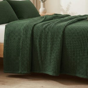 Op de afbeelding: Een donker bosgroene sprei en bijpassende kussenslopen met een wafelstructuur. De stof heeft een duidelijke rasterachtige textuur over het gehele oppervlak van het beddengoed, wat zorgt voor een uniforme en tactiele uitstraling.
