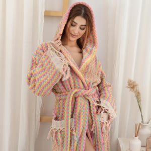 May include: A pink, yellow, and blue patterned hooded bathrobe with a tie belt and fringe trim.