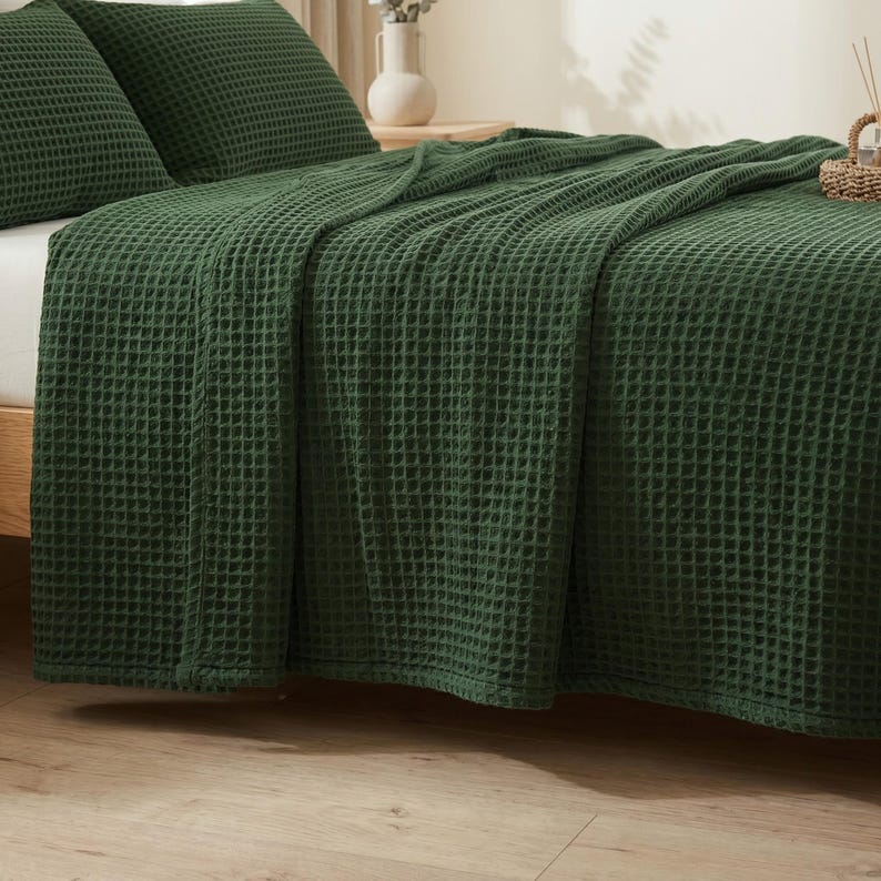 Op de afbeelding: Een donker bosgroene sprei en bijpassende kussenslopen met een wafelstructuur. De stof heeft een duidelijke rasterachtige textuur over het gehele oppervlak van het beddengoed, wat zorgt voor een uniforme en tactiele uitstraling.