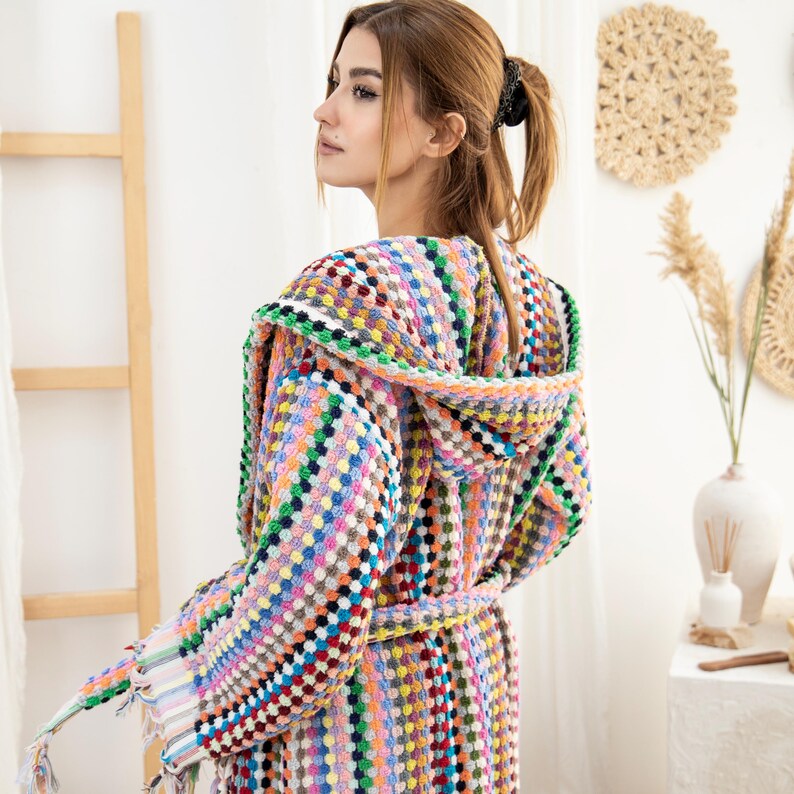 May include: A colorful hooded robe with a geometric pattern in shades of pink, blue, green, yellow, and orange. The robe has a tie belt and a fringed hem.