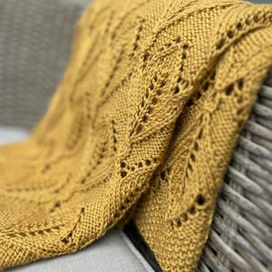 May include: A mustard yellow knitted throw blanket with a lacy pattern. The blanket is draped over a wicker chair.
