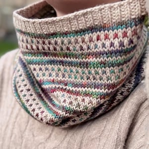 May include: A hand-knitted cowl in a mix of colors, including beige, teal, purple, and red. The cowl features a textured stitch pattern and is made of soft yarn. This cozy accessory is perfect for cold weather.