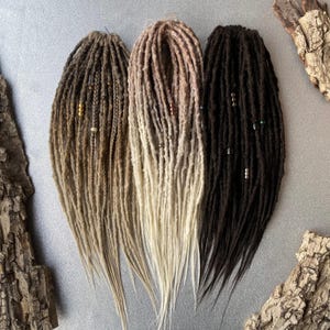Pode incluir: Três conjuntos de dreadlocks sintéticas em marrom, loiro e marrom claro. Cada conjunto tem contas tecidas nas dreadlocks.