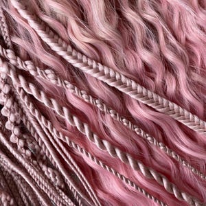 May include: A close-up of pink hair extensions with a variety of braids and twists. The hair is soft and wavy, and the braids are a variety of thicknesses.