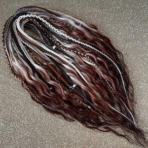 May include: A collection of handmade dreadlocks in shades of brown, white, and grey. The dreadlocks have a wavy texture and are decorated with small beads and accents. The style is bohemian and natural, suitable for alternative hairstyles.