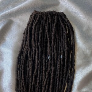 May include: A close-up of black dreadlocks with two black beads.