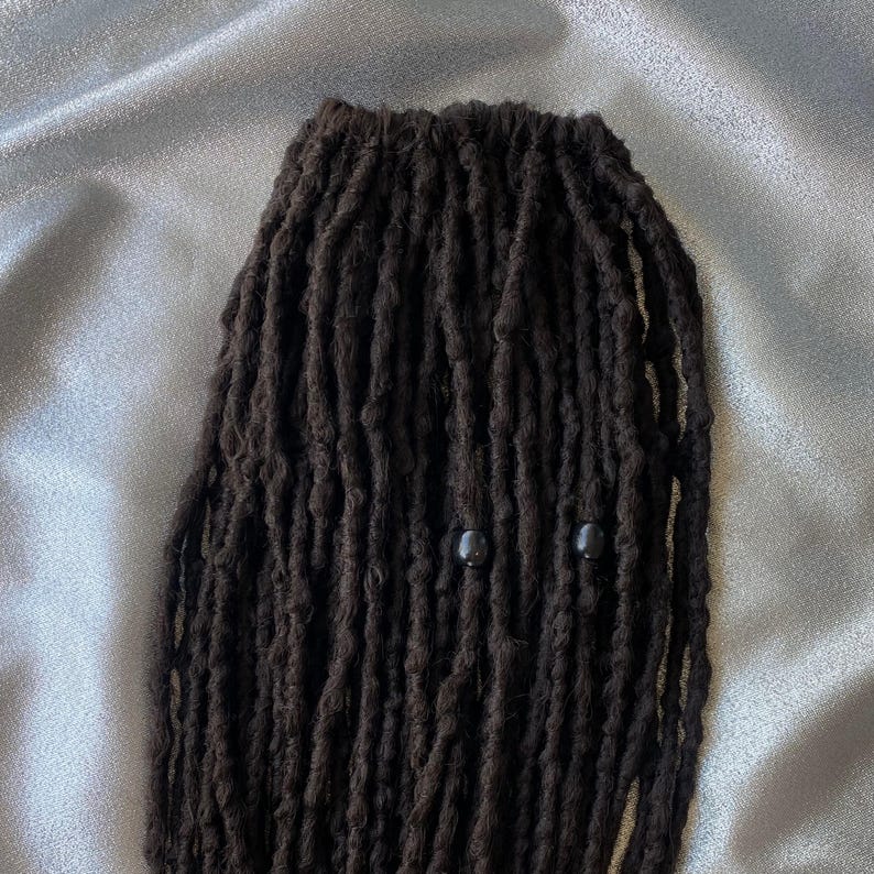 May include: A close-up of black dreadlocks with two black beads.