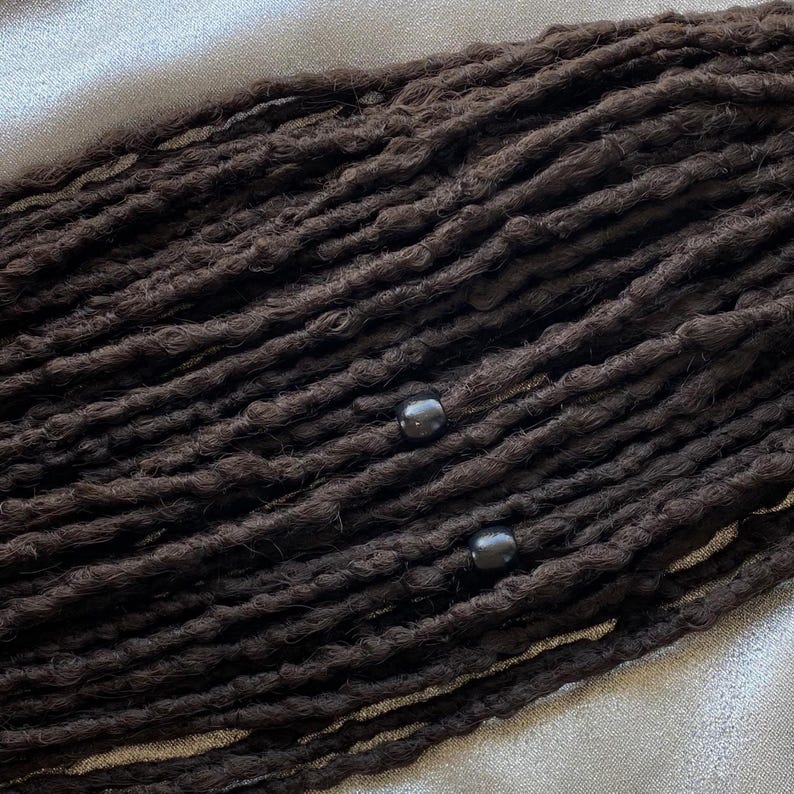 May include: A close-up of a set of black dreadlocks with black beads. The dreadlocks are arranged in rows and are very thick.