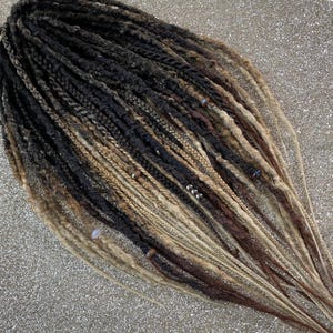 May include: A collection of handmade dreadlocks in various shades of brown, black, and blonde. The dreads are intricately braided and feature decorative beads. The color gradient creates a natural, textured appearance, suitable for alternative hairstyles.