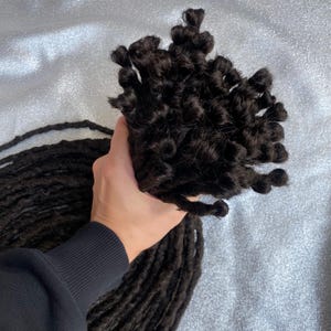 May include: A bundle of dark brown synthetic dreadlocks, approximately 20 inches long, with the ends curled into tight coils.