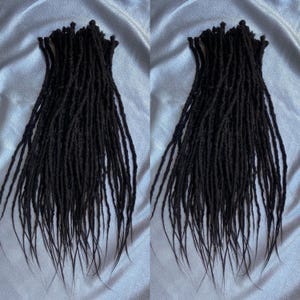 May include: Two sets of black synthetic dreadlocks, each set containing approximately 50 dreads. The dreadlocks are long and straight, with a slightly textured surface.