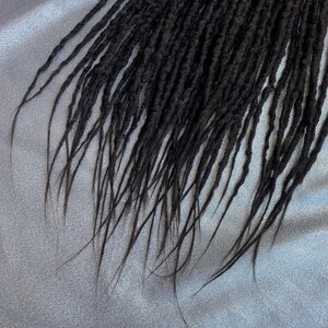 May include: A close-up of a set of black dreadlocks, showing the texture and detail of the individual strands.