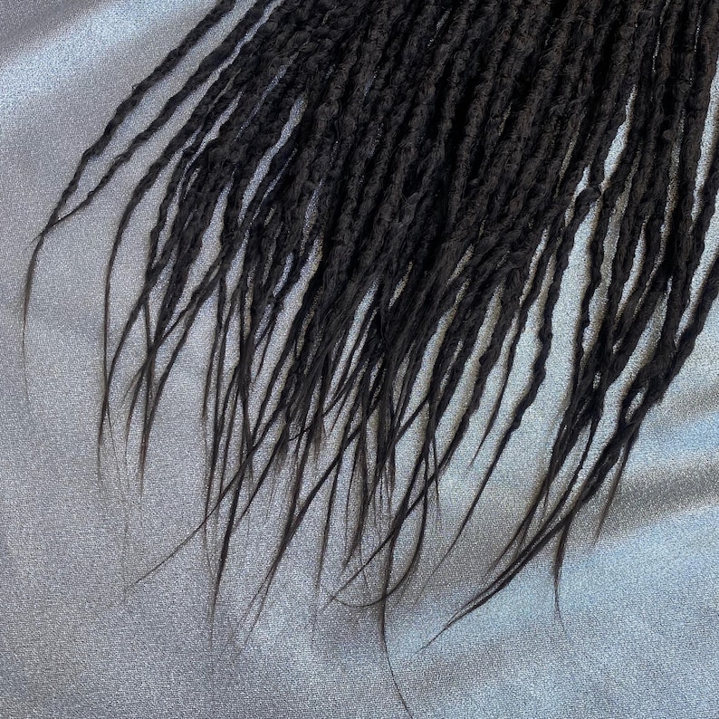 May include: A close-up of a set of black dreadlocks, showing the texture and detail of the individual strands.