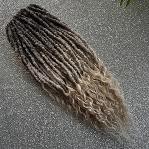 Könnte beinhalten: Ein Set langer, synthetischer Dreadlocks in einem hellbraunen und blonden Ombre-Farbton. Die Dreadlocks sind lockig und haben eine strukturierte Oberfläche.
