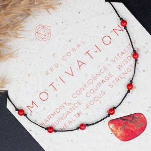 Può includere: Collana di corallo rosso con cordoncino nero e perline rosse. La collana è su una carta bianca con le parole "RED CORAL MOTIVATION" e "ROOT CHAKRA SACRAL CHAKRA WATER & FIRE".