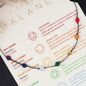 May include: A chakra bracelet featuring seven colourful stones, including red coral, yellow aventurine, citrine, malachite, aquamarine, lapis lazuli, and amethyst. The bracelet is displayed on a white card with descriptions of the seven chakras and their meanings. The card also includes the text "7 Chakra Balance" and "Buy Set & Get Extra 10% Off".