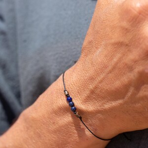 May include: A simple bracelet with a black cord and three dark blue beads.