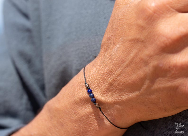 May include: A simple bracelet with a black cord and three dark blue beads.