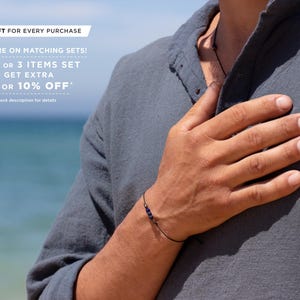 May include: A person wearing a dark gray shirt with a black cord necklace and a black string bracelet with small blue beads. The text "FREE GIFT FOR EVERY PURCHASE" is at the top of the image. The text "SAVE MORE ON MATCHING SETS! BUY 2 OR 3 ITEMS SET & GET EXTRA 5% OR 10% OFF*" is below the first line of text. The text "*Check description for details" is below the second line of text.
