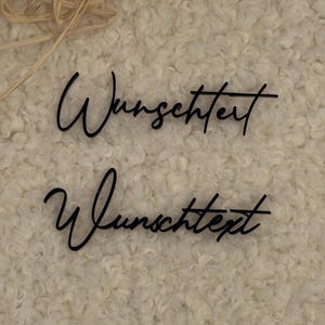 Könnte beinhalten: Zwei schwarze Acrylschilder mit dem deutschen Wort Wunschtext in einer Schreibschrift. Die Buchstaben sind dünn und miteinander verbunden und in einer gestapelten Anordnung dargestellt. Die Schilder bestehen aus glattem, dunklem Material.